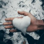 A heart-shaped snow piece held in a hand on a snowy day symbolizes winter love.