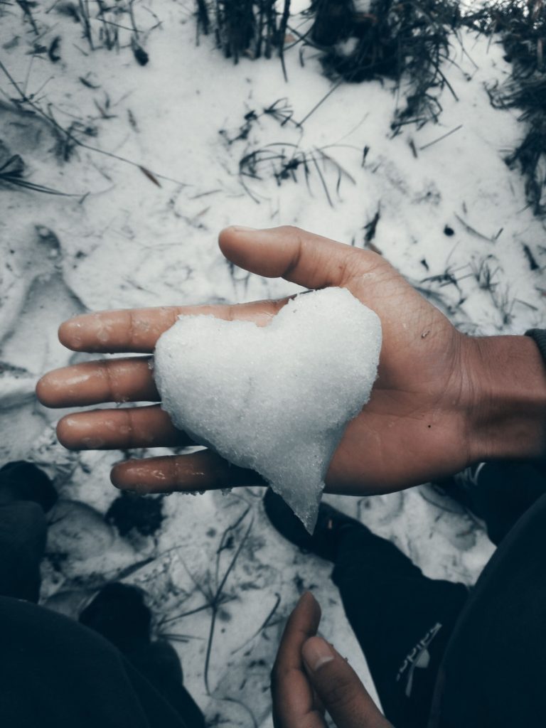 A heart-shaped snow piece held in a hand on a snowy day symbolizes winter love.